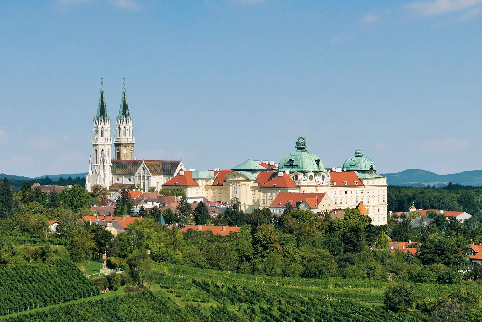 Panoramablick auf das Stift Klosterneuburg mit grünen Weinbergen im Vordergrund.