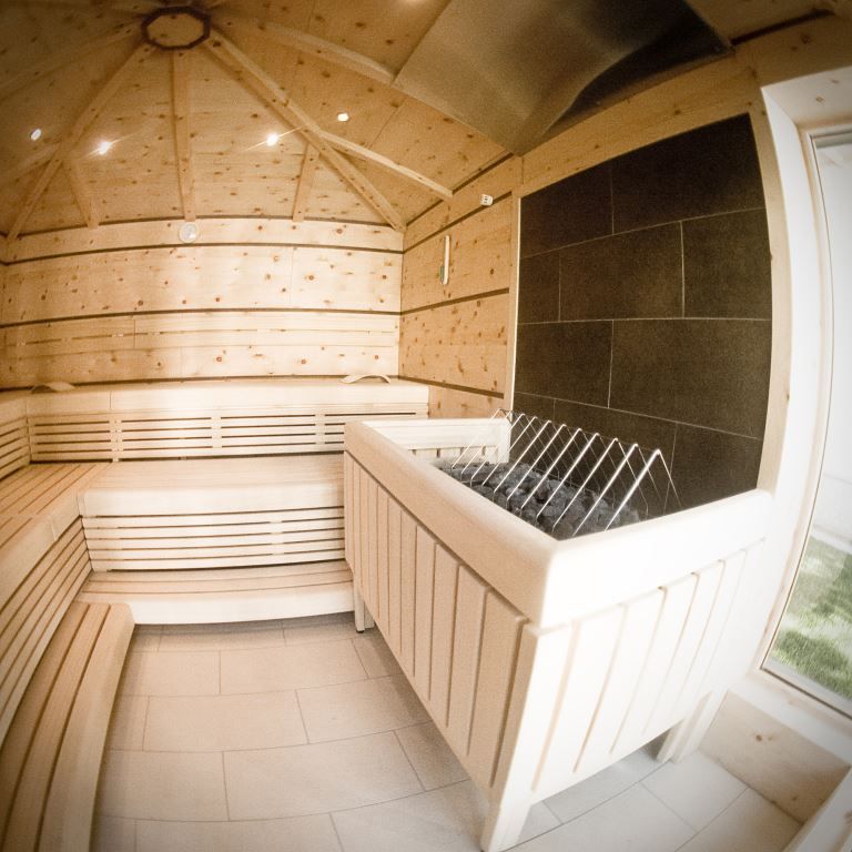 Innenansicht einer modernen Sauna mit Holzbänken und Ofen.