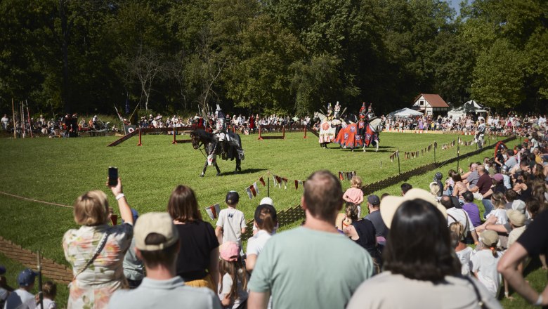 Ritterturnier im Schlosspark Laxenburg mit Zuschauern und Rittern auf Pferden.