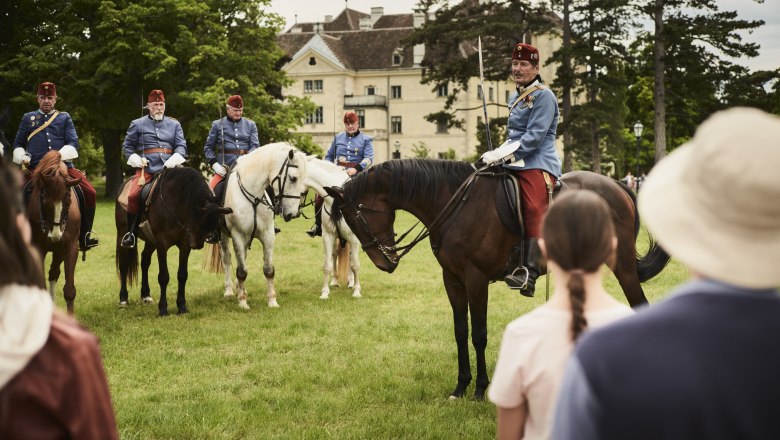 Reiter in historischen Uniformen auf Pferden vor einem Schloss.