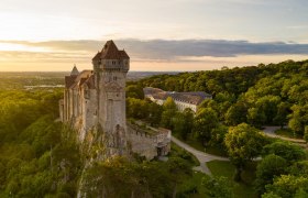 Burg Liechtenstein auf einem H&uuml;gel, umgeben von Wald, bei Sonnenuntergang.
