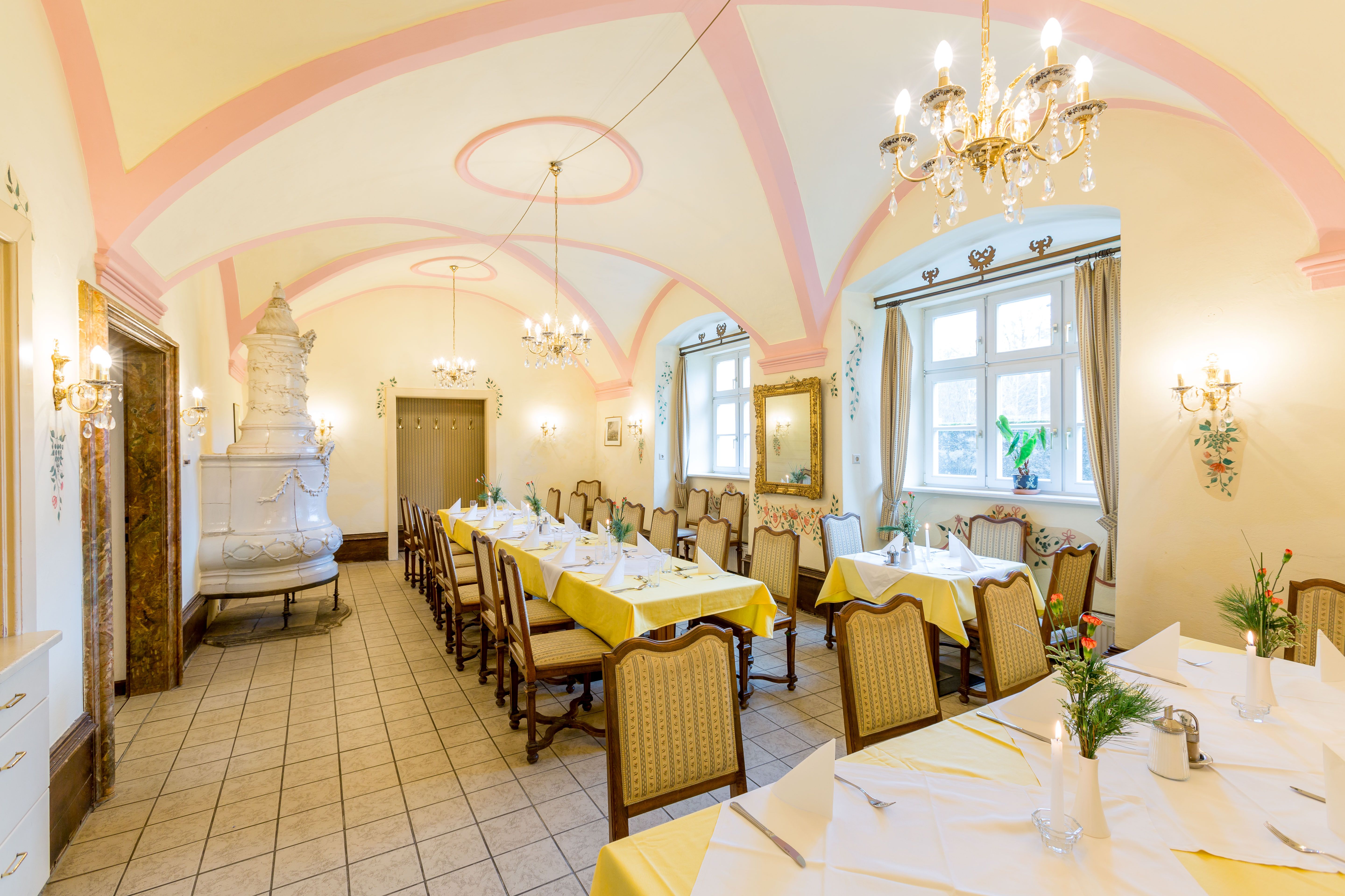 Eleganter Speisesaal mit gedeckten Tischen, Kronleuchtern und Kachelofen.